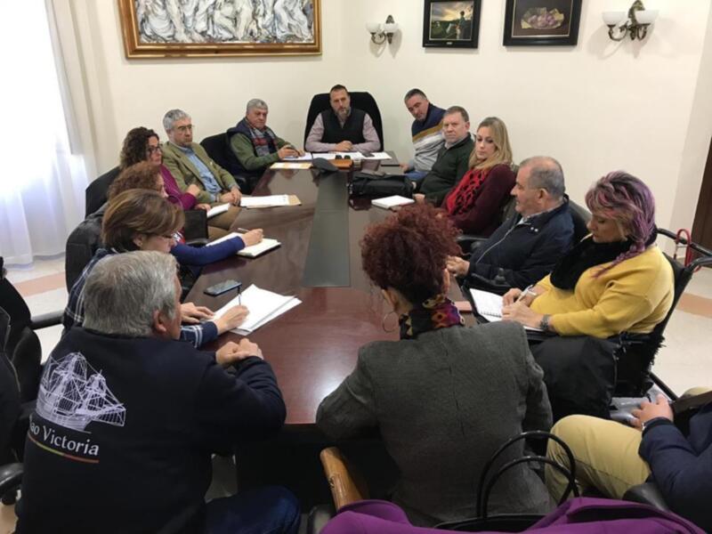 Reunión de trabajo en una sala con sillas y mesas, participantes sentados alrededor del escritorio.