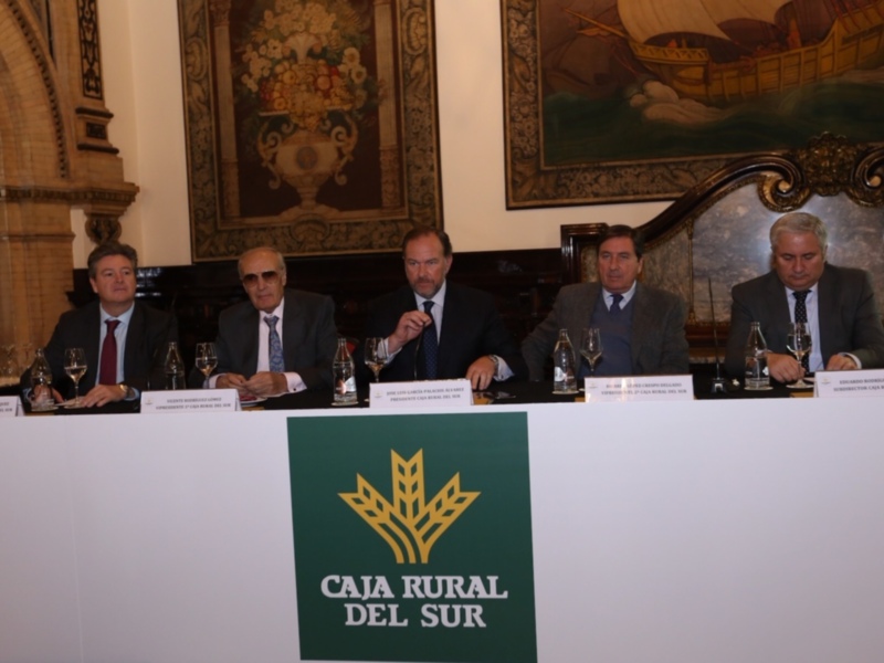 Presentación de Caja Rural del Sur en un evento formal, con miembros de la organización sentados en una mesa y el logo de la entidad en primer plano.