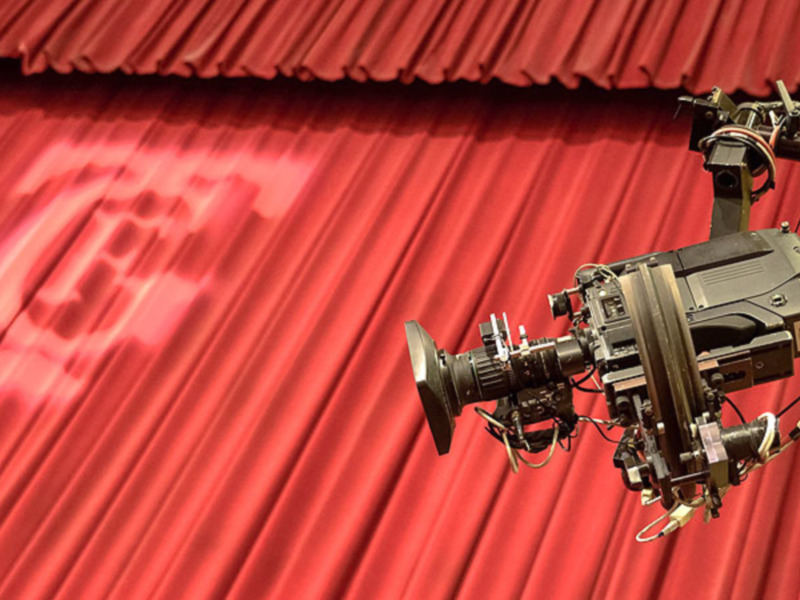 Una cámara de cine profesional en un escenario con telón rojo.