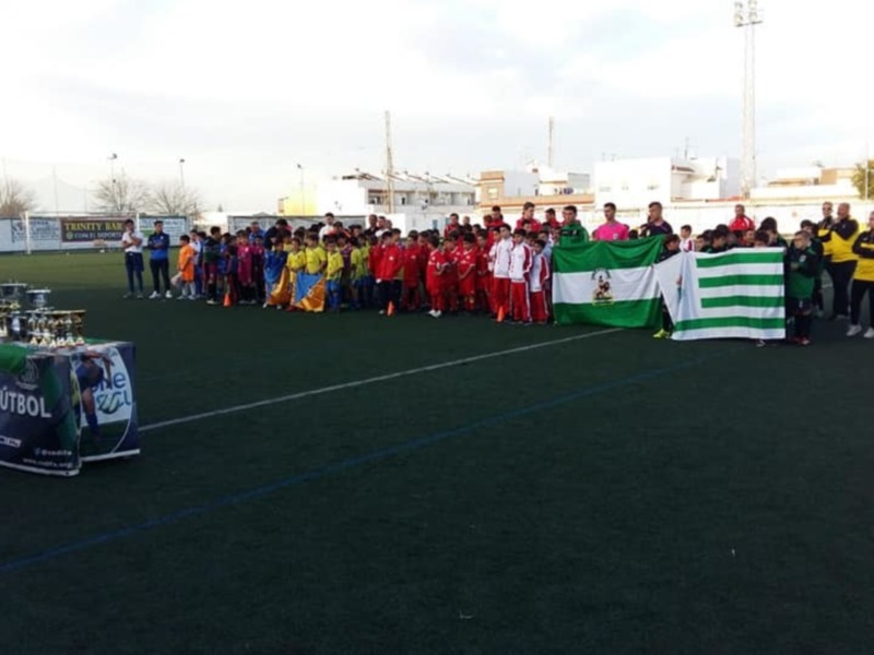 Equipo de fútbol escolar posando con trofeos y bandera en un campo de fútbol.