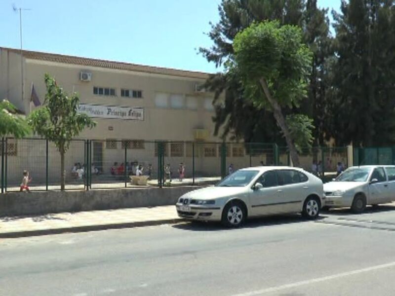 Edificio blanco con toldos verdes, árboles y personas en el patio.
