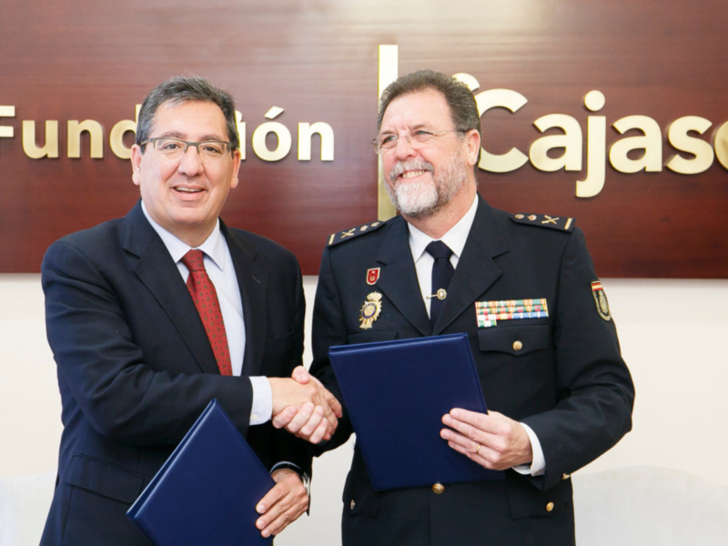 Dos hombres, uno en traje y el otro en uniforme militar, firmando un documento en una oficina formal.