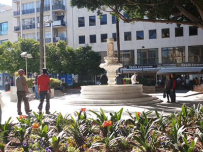 Plaza con fuente, flores y edificios en el fondo, un ambiente urbano tranquilo.