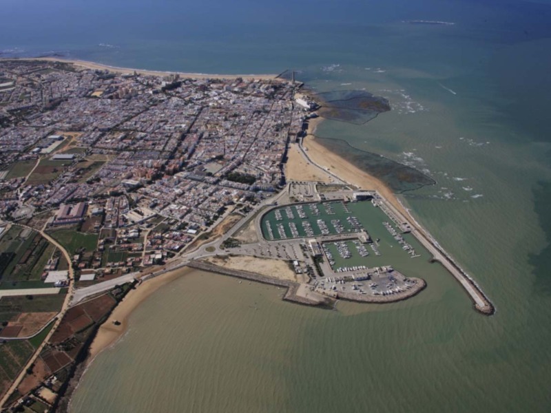 Aerial view of a coastal town with a marina and a sandy beach.