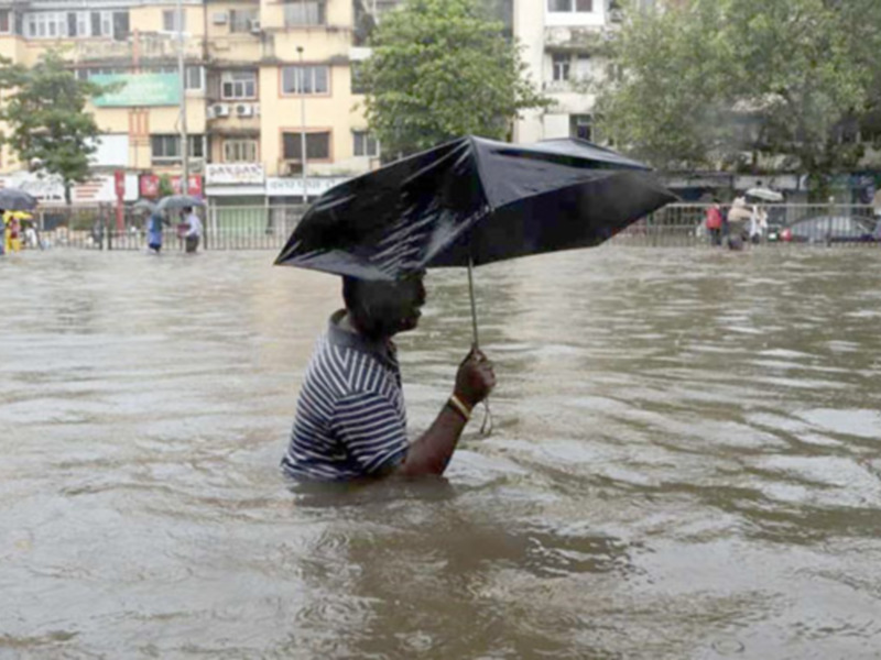 Un hombre camina por una calle inundada con un paraguas negro. La imagen muestra la intensidad de las lluvias torrenciales que han causado una gran cantidad de agua en el suelo.