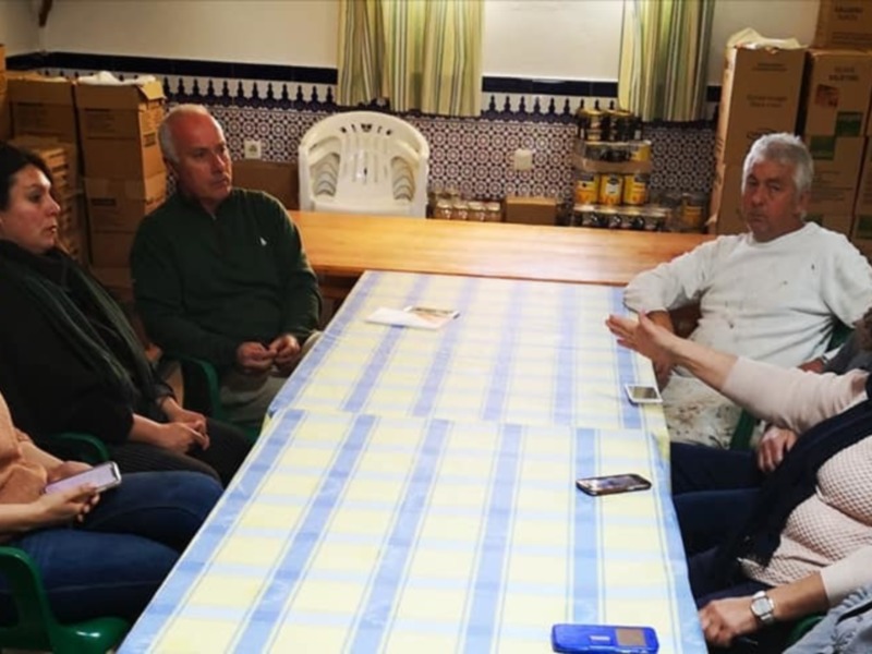 Una familia reunida en una cocina con mesa cubierta, sillas verdes y estanterías de madera.