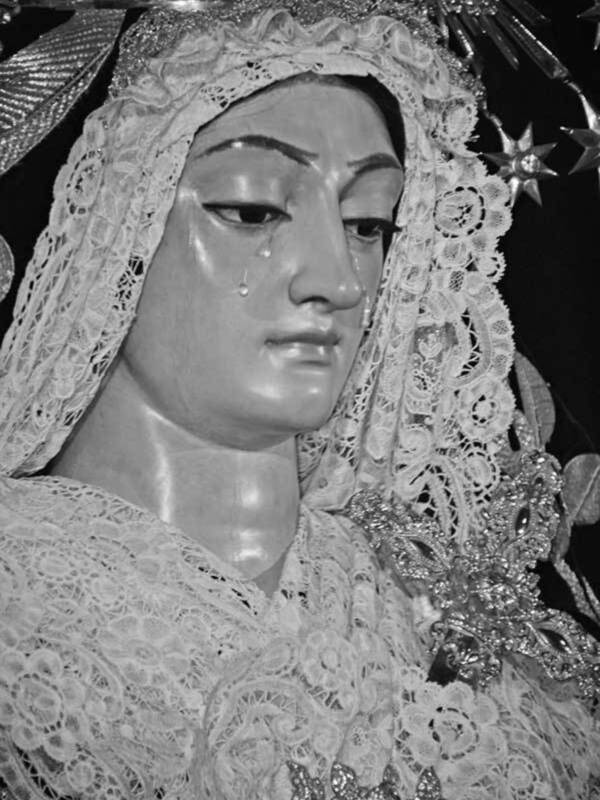 Una figura religiosa vestida con un manto de encaje y una corona. La escena parece ser parte de una procesión o celebración religiosa, con detalles dorados y cristales en la corona.