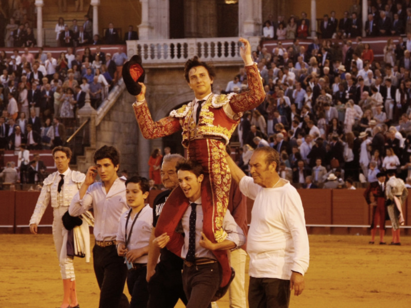 A matador in traditional bullfighting attire is being carried by a group of men in a stadium filled with spectators.