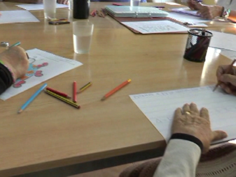 Una persona dibuja en un papel con lápices de colores sobre una mesa con otros materiales de oficina.