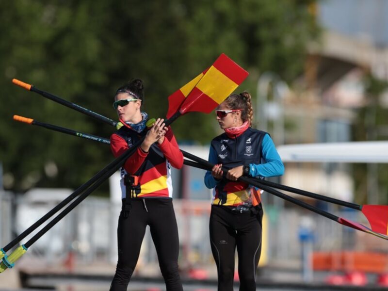 Dos personas con cascos y cascos de remo en una competición de remo en el agua. La escena se centra en la preparación de los deportistas para el evento.