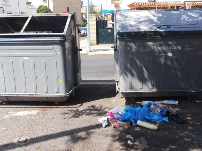 Dos contenedores de basura en un aparcamiento con residuos no reciclados al lado.