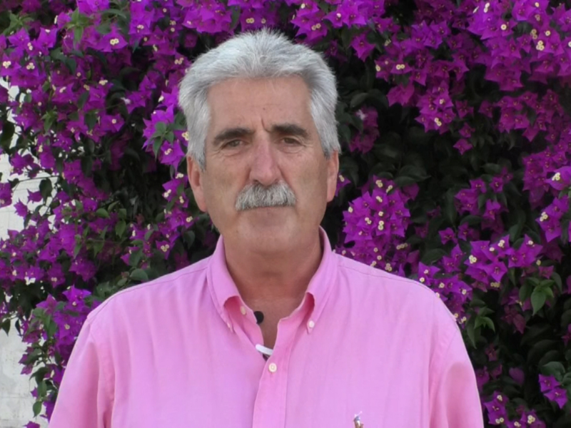 Hombre sonriente frente a una hermosa mata de flores púrpuras.