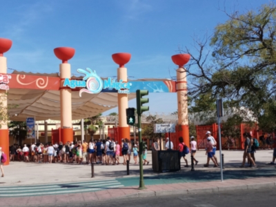 Puerta de entrada a un parque temático con torres rojas y el nombre "El Mirador" en letras grandes. La entrada está rodeada de árboles y el cielo es azul claro.