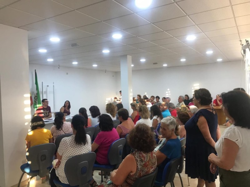 Asamblea de mujeres en una sala de reuniones, escuchando a una ponente en el extremo izquierdo.