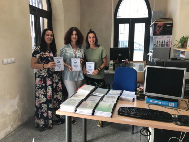 Tres personas posan con libros en una oficina.