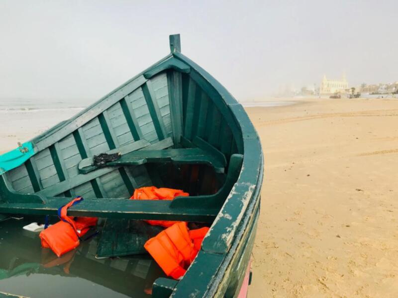 Barco verde en la playa con natación salvavidas rojas. Fondo de arena y cielo claro.