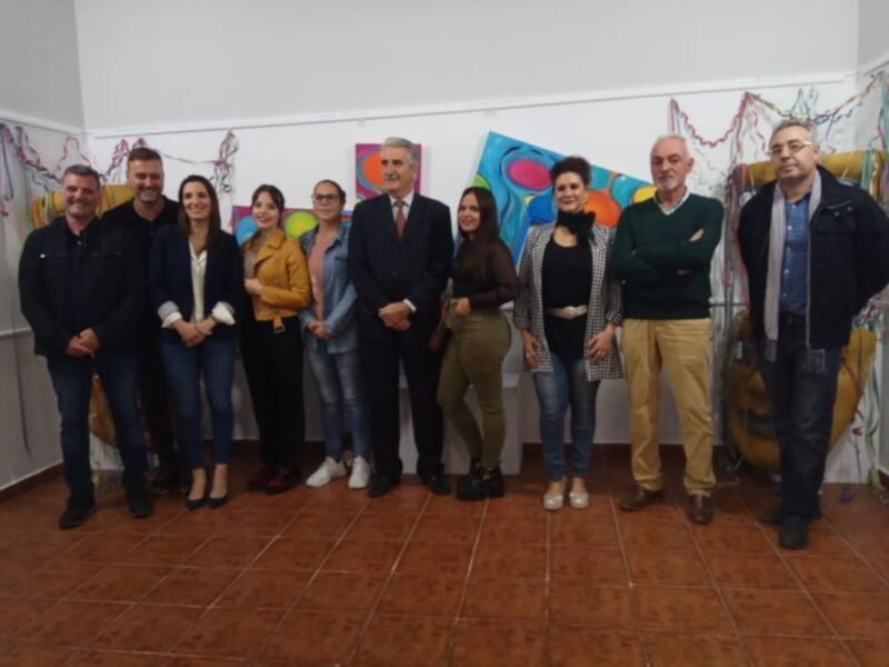 Grupo de personas posando en una exposición de arte junto a obras abstractas vibrantes.