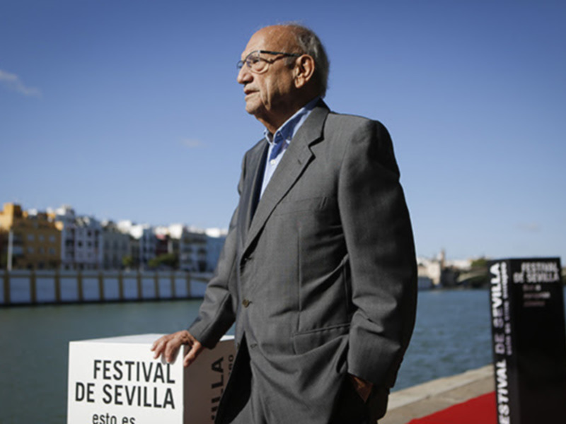 Festival de Sevilla, hombre en traje frente al río con cartel del festival.