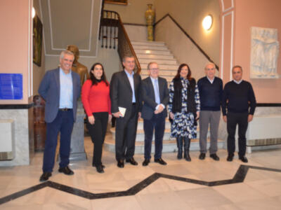 Una imagen de seis personas posando en un pasillo con escaleras y decoración. La escena parece ser formal, posiblemente en un evento o reunión empresarial.