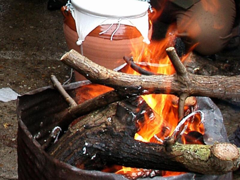 Un fuego en un recipiente de metal, con troncos y una cesta blanca.