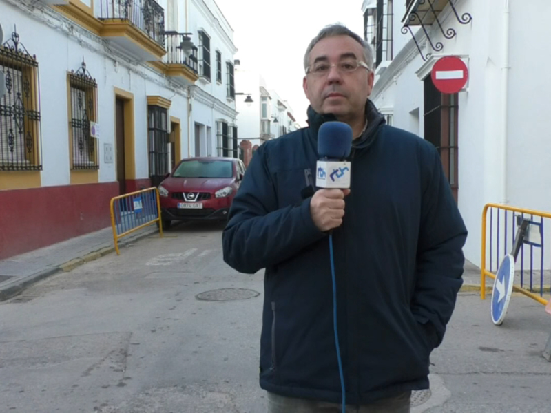 Reportaje fotográfico de un locutor en una calle con señales de tráfico y vehículos cercanos.
