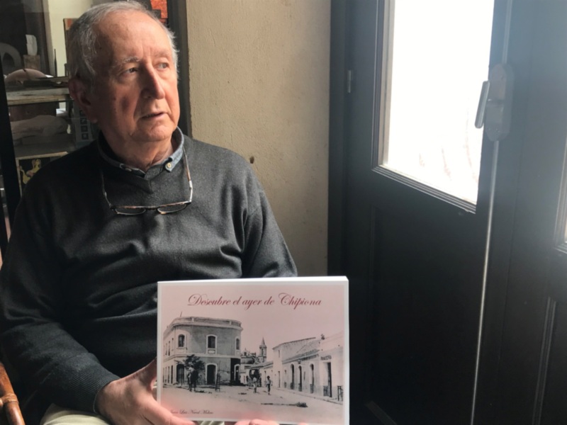 Un hombre en una sala con una ventana, sosteniendo un libro titulado "Descubre el ayer de Chippa". La imagen muestra una casa antigua en la portada del libro.