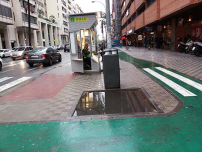 Una imagen de una calle con un teléfono público, edificios a ambos lados y un poste de luz en el centro.