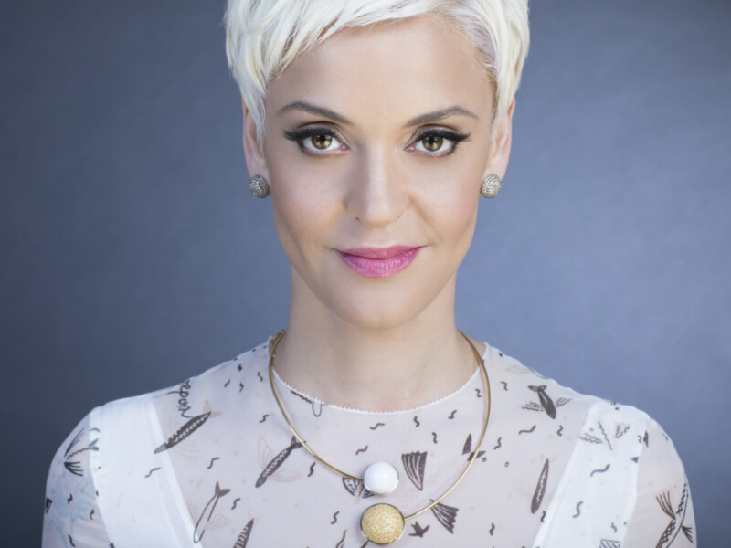 Retrato de mujer con cabello corto y rubio, maquillaje sofisticado y joyería elegante.