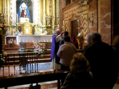 Interior de una iglesia con altares ornamentados y personas participando en una ceremonia religiosa.