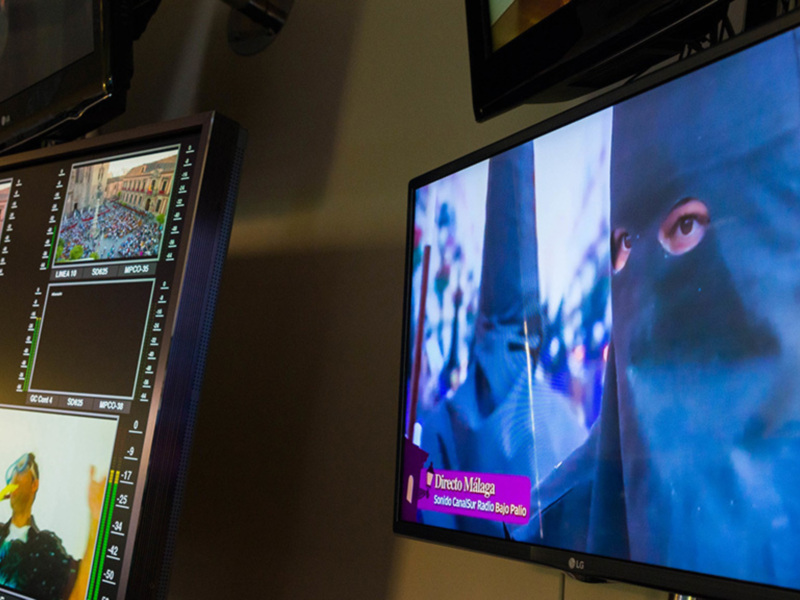 Dos monitores de televisión en una sala de producción, uno muestra un programa de televisión mientras el otro muestra una escena con una persona cubierta por un manto oscuro.