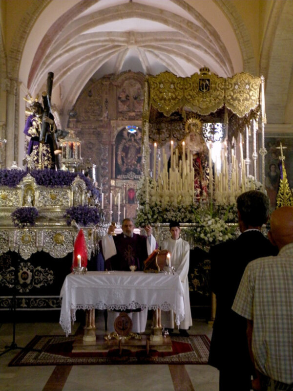 Interior de una iglesia con un altar dorado, estatuas religiosas y velas encendidas.