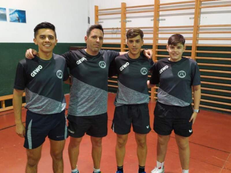 Tres jóvenes deportistas posan juntos en una sala de deportes, todos vestidos con uniformes de entrenamiento de la marca GEWO. La sala tiene paredes de madera y un suelo de baldosas rojas, creando un ambiente deportivo y motivador.
