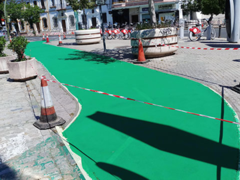 Un camino de asfalto con una línea verde curva en el centro, rodeado de conos y barreras de seguridad.