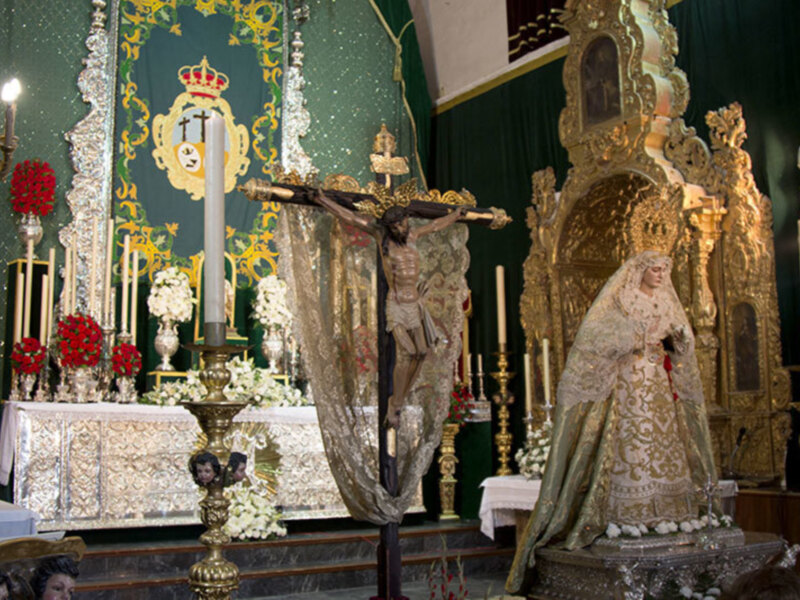 Altar de la iglesia con estatuas religiosas y flores en un ambiente festivo. La imagen muestra una escena religiosa con elementos decorativos y una estructura de altar.