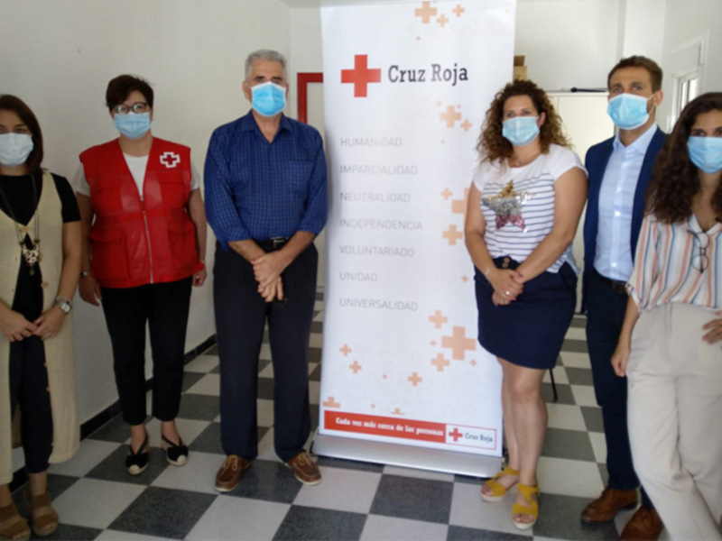 Grupo de personas con máscaras faciales en una reunión frente a un banner de Cruz Roja.