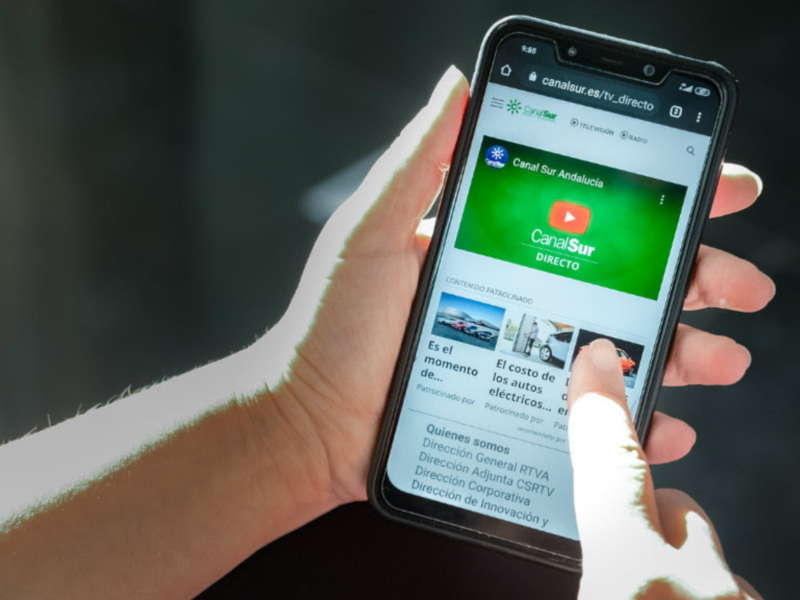 Mano sosteniendo un teléfono móvil con la pantalla de Canal Sur Andalucía en directo.