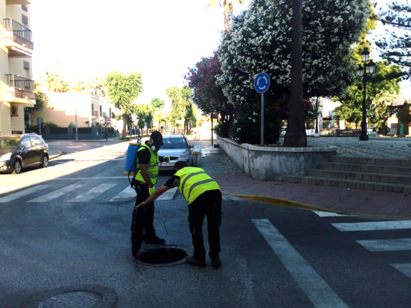 Un trabajador de la limpieza en uniforme amarillo y negro está limpiando una mancha en el asfalto de una calle.