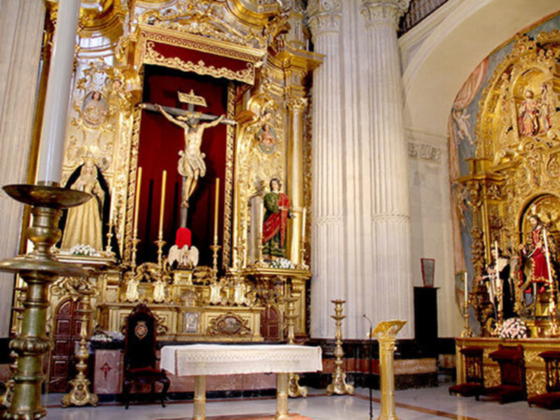 Altar de una iglesia con estatuas doradas y un crucificado en el centro, rodeado de velas y candelabros.