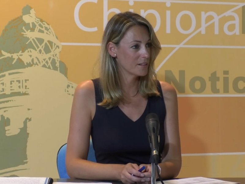 A una mujer sentada en un escritorio, con un fondo amarillo que incluye el logotipo de la Casa Blanca y la palabra "Noticias". La mujer parece estar en una conferencia o rueda de prensa, posiblemente dando un discurso.
