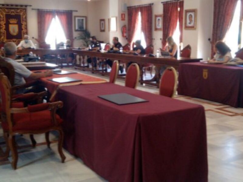 Sala de reuniones con mesas cubiertas y sillas rojas, decoración con banderas y carteles en las paredes.