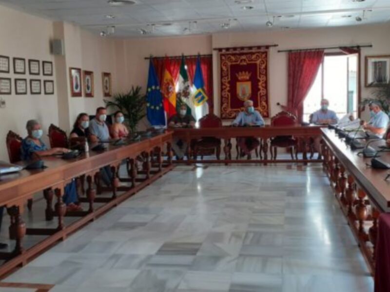 Reunión de trabajo en una sala de conferencias con personas sentadas en mesas y banderas de la UE y España en el fondo.