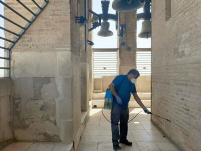 Un hombre usa un atomizador para limpiar una pared de ladrillo en el interior de un edificio histórico. La imagen muestra detalles arquitectónicos y la acción de limpieza.