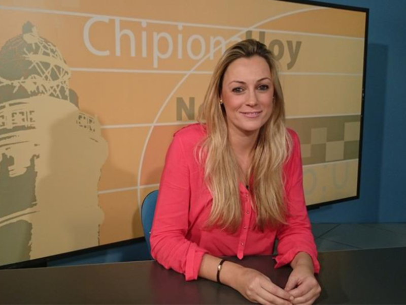 Una mujer en un estudio de televisión con un fondo de escarabajo y un logo en el fondo.