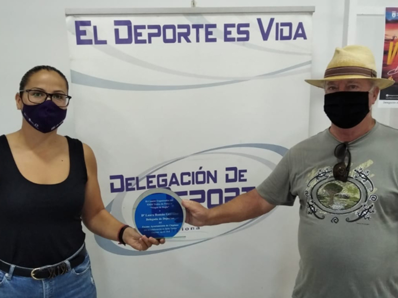 Dos personas sostienen una placa de reconocimiento frente a un fondo con el texto "El Deporte es Vida" y una imagen de una película.