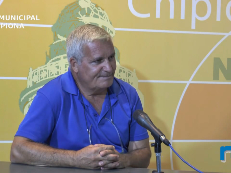 Hombre hablando en una conferencia de prensa frente a un fondo amarillo con el logo de RTV Municipal y Chipiona.