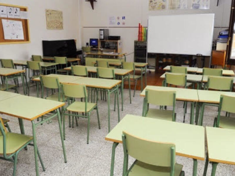 Clase de matemáticas con mesas verdes, sillas verdes y un proyector en la pared.