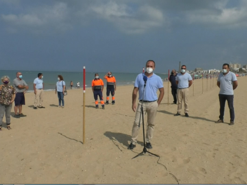 Personas en la playa con máscaras y uniformes, posiblemente trabajadores ambientales o de salud.