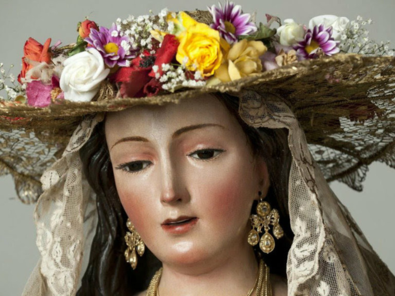 Detalle de una figura religiosa con un sombrero elaborado y flores en la cabeza.