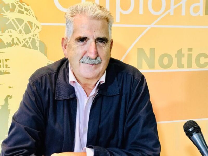 El hombre está en una conferencia de prensa, con un fondo amarillo y letras blancas que parece ser parte de una publicidad o logotipo.