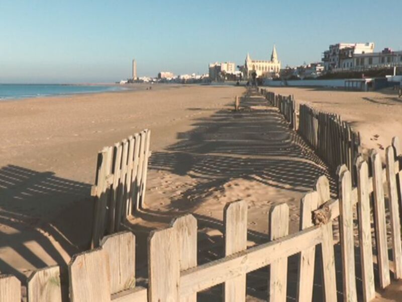 Playa de Cádiz con vistas al mar y edificios en el horizonte.